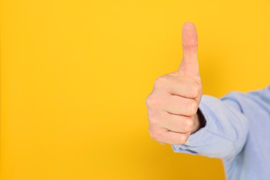 Man showing thumb up on orange background, closeup. Space for text