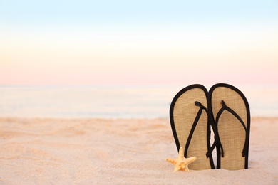 Photo of Stylish flip flops on sand near sea, space for text. Beach accessories