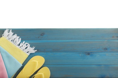Light blue wooden surface with beach towel and flip flops on white background, top view. Space for text