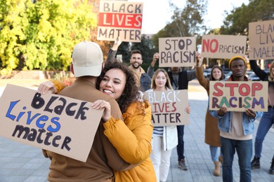 Photo of African American woman hugging man and holding sign with phrase Black Lives Matter outdoors during anti racism protest