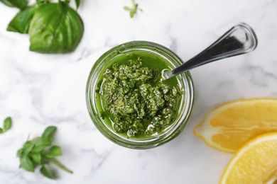 Photo of Homemade basil pesto sauce in glass jar on table, top view