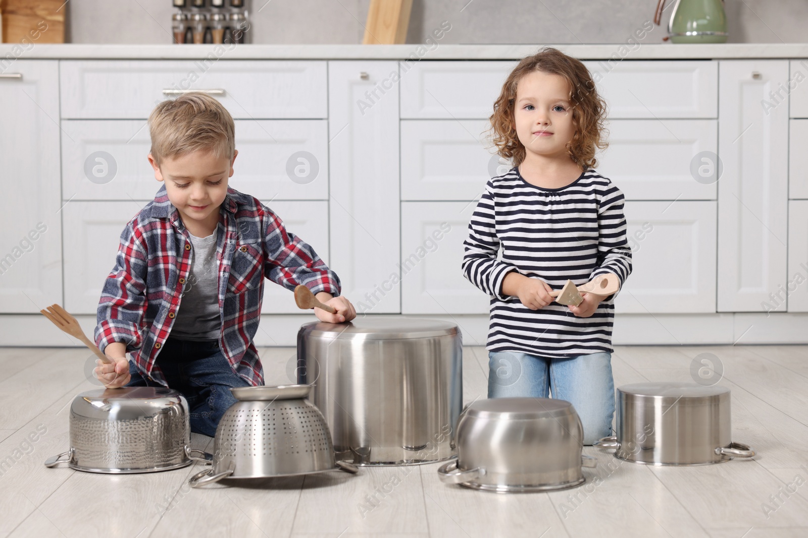 Photo of Little children pretending to play drums on pots in kitchen