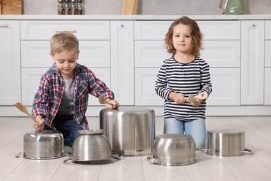 Little children pretending to play drums on pots in kitchen