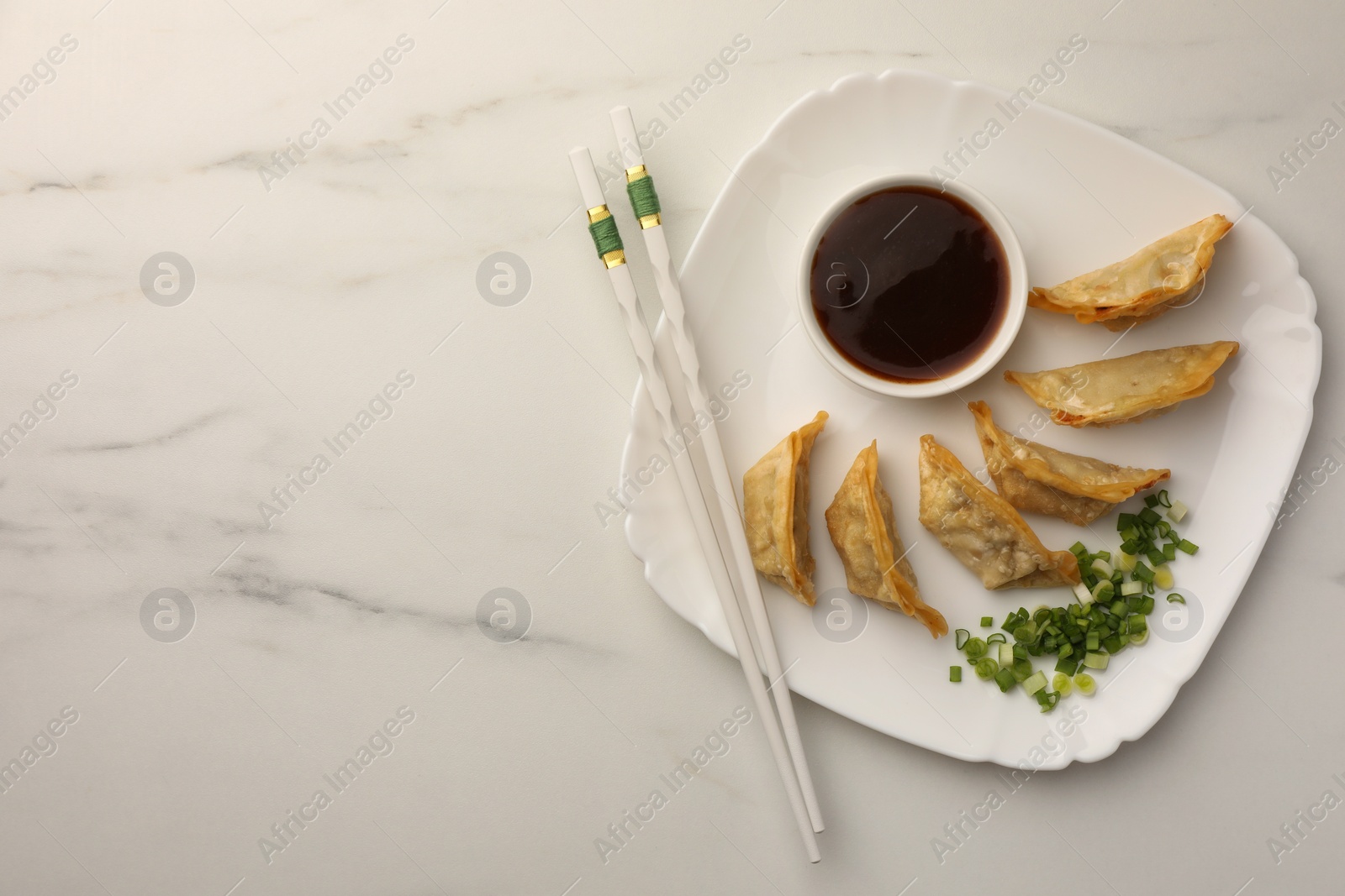 Photo of Delicious gyoza (asian dumplings) with soy sauce, green onions and chopsticks on white marble table, top view. Space for text