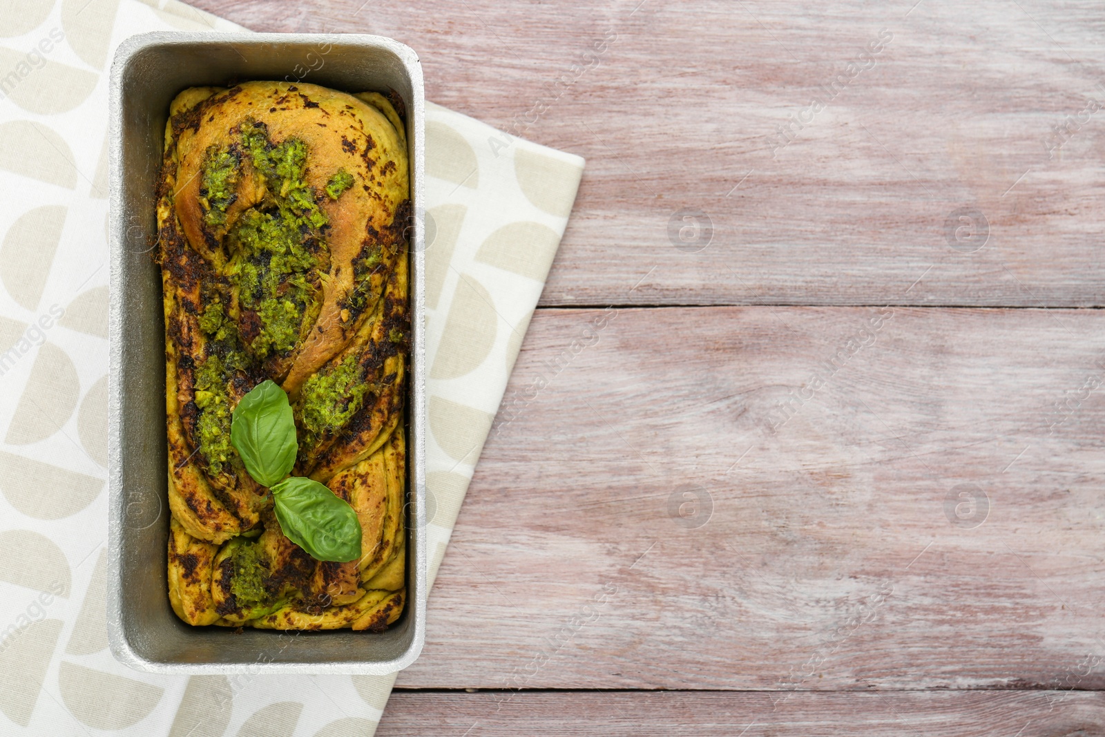 Photo of Freshly baked pesto bread with basil in loaf pan on wooden table, top view. Space for text