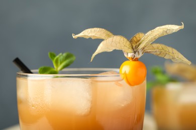 Photo of Refreshing cocktail decorated with physalis fruit on grey background, closeup