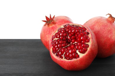 Photo of Fresh pomegranates on black wooden table against white background, space for text