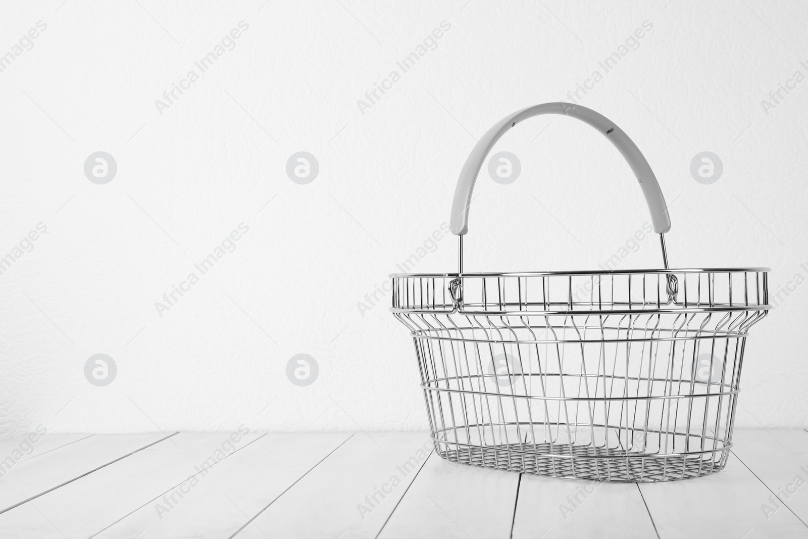 Photo of Empty metal shopping basket on light wooden table against white background. Space for text