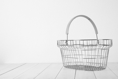 Photo of Empty metal shopping basket on light wooden table against white background. Space for text