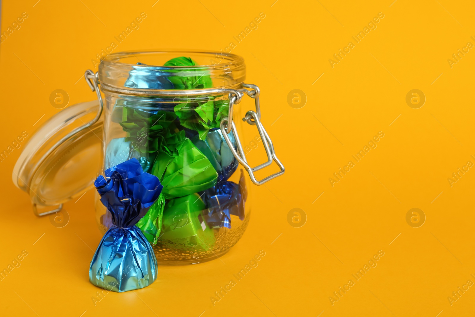 Photo of Candies in colorful wrappers on yellow background. Space for text