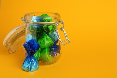 Photo of Candies in colorful wrappers on yellow background. Space for text