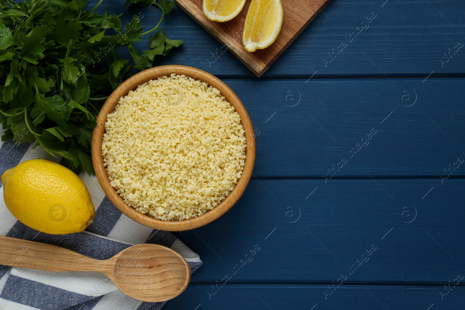 Photo of Tasty couscous and ingredients on blue wooden table, flat lay. Space for text