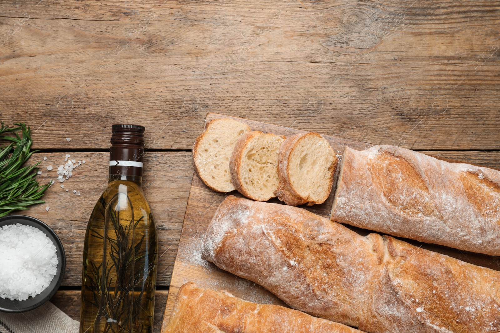 Photo of Delicious French baguettes with rosemary and oil on wooden table, flat lay