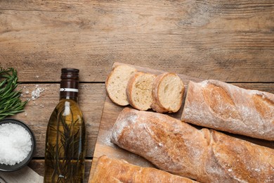 Delicious French baguettes with rosemary and oil on wooden table, flat lay