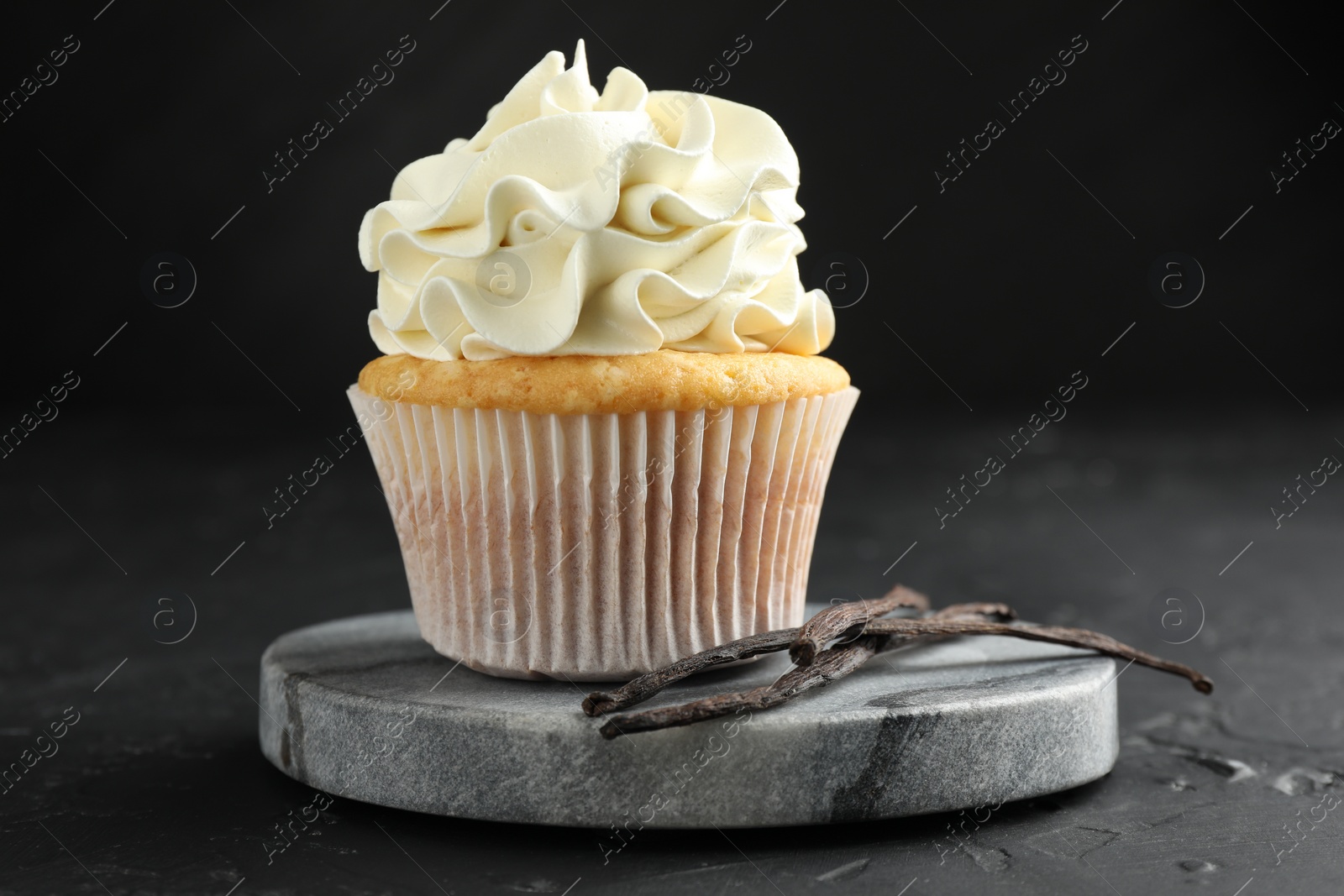 Photo of Tasty cupcake with cream and vanilla pods on black table, closeup