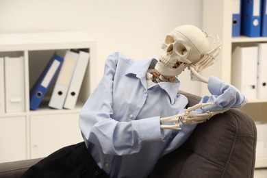 Waiting concept. Human skeleton sitting in armchair at office