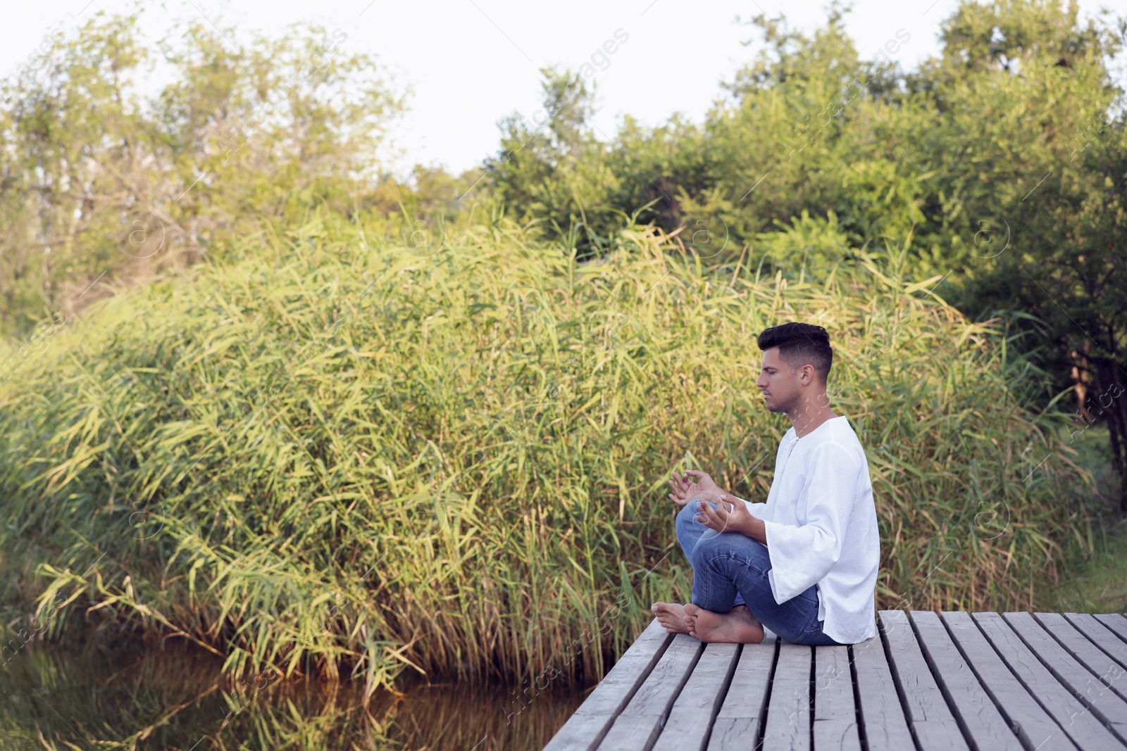 Photo of Man meditating on wooden pier near river. Space for text