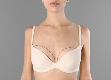 Photo of Young woman with marks on breast for cosmetic surgery operation against gray background, closeup