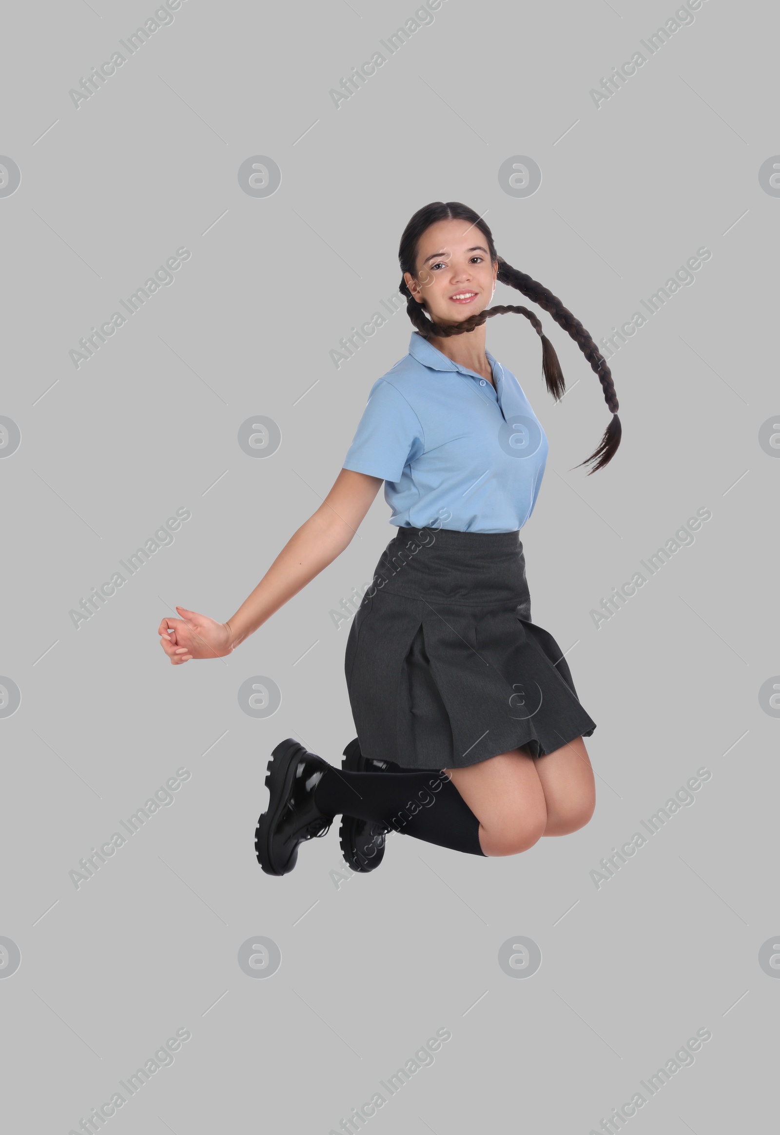 Image of Happy cute girl in school uniform jumping on grey background
