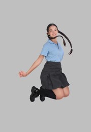 Happy cute girl in school uniform jumping on grey background