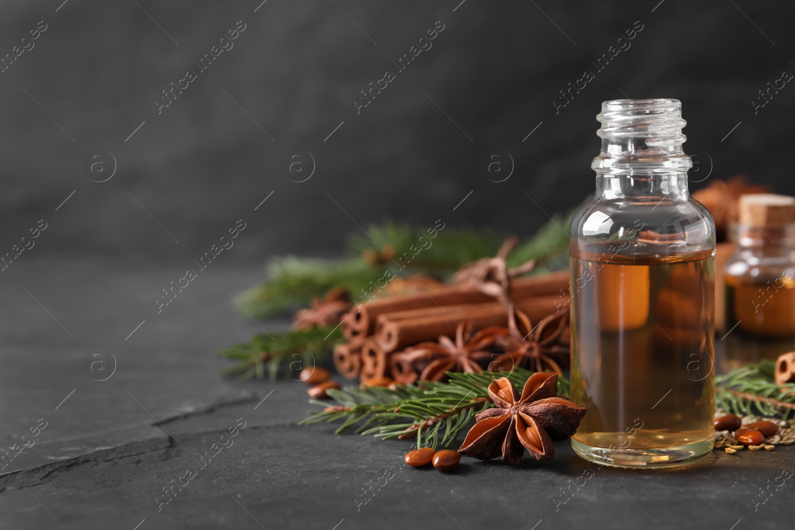 Photo of Bottle of essential oil, anise, cinnamon and fir tree branches on black table. Space for text