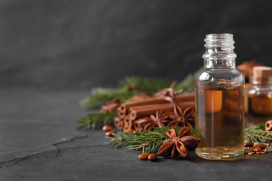 Bottle of essential oil, anise, cinnamon and fir tree branches on black table. Space for text