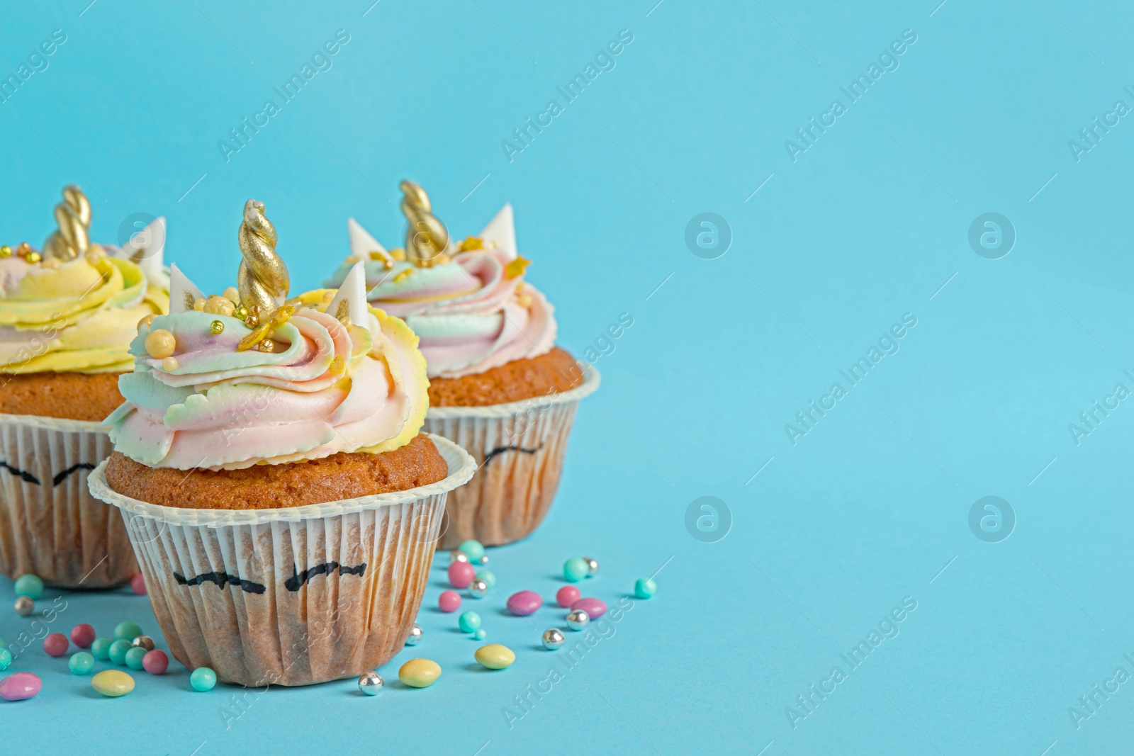 Photo of Cute sweet unicorn cupcakes on light blue background, space for text