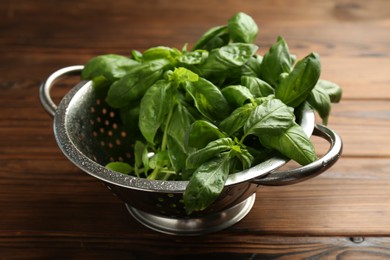 Photo of Metal colander with fresh basil leaves on wooden table, closeup