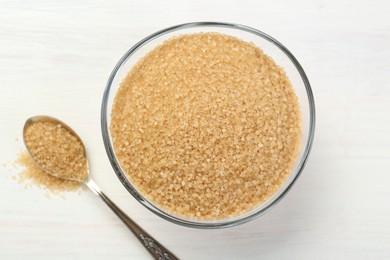 Photo of Brown sugar in bowl and spoon on white wooden table, flat lay