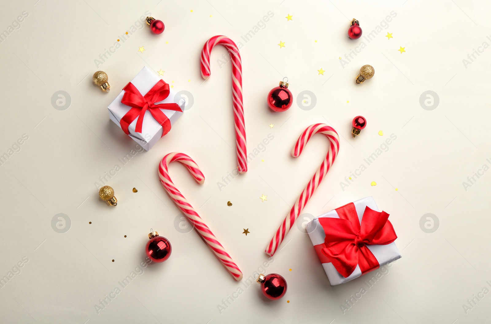 Photo of Candy canes, Christmas balls and gift boxes on beige background, flat lay