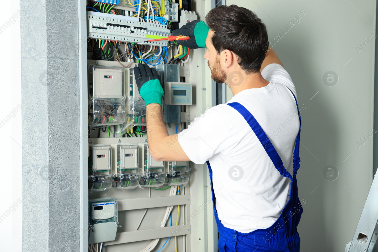 Photo of Electrician repairing fuse box with screwdriver indoors