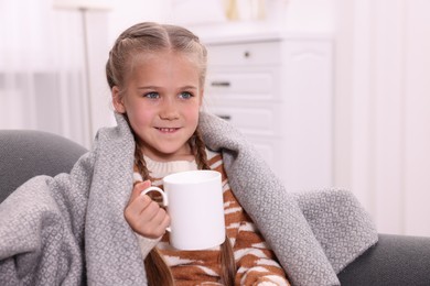 Photo of Happy girl under plaid with white ceramic mug on sofa at home, space for text