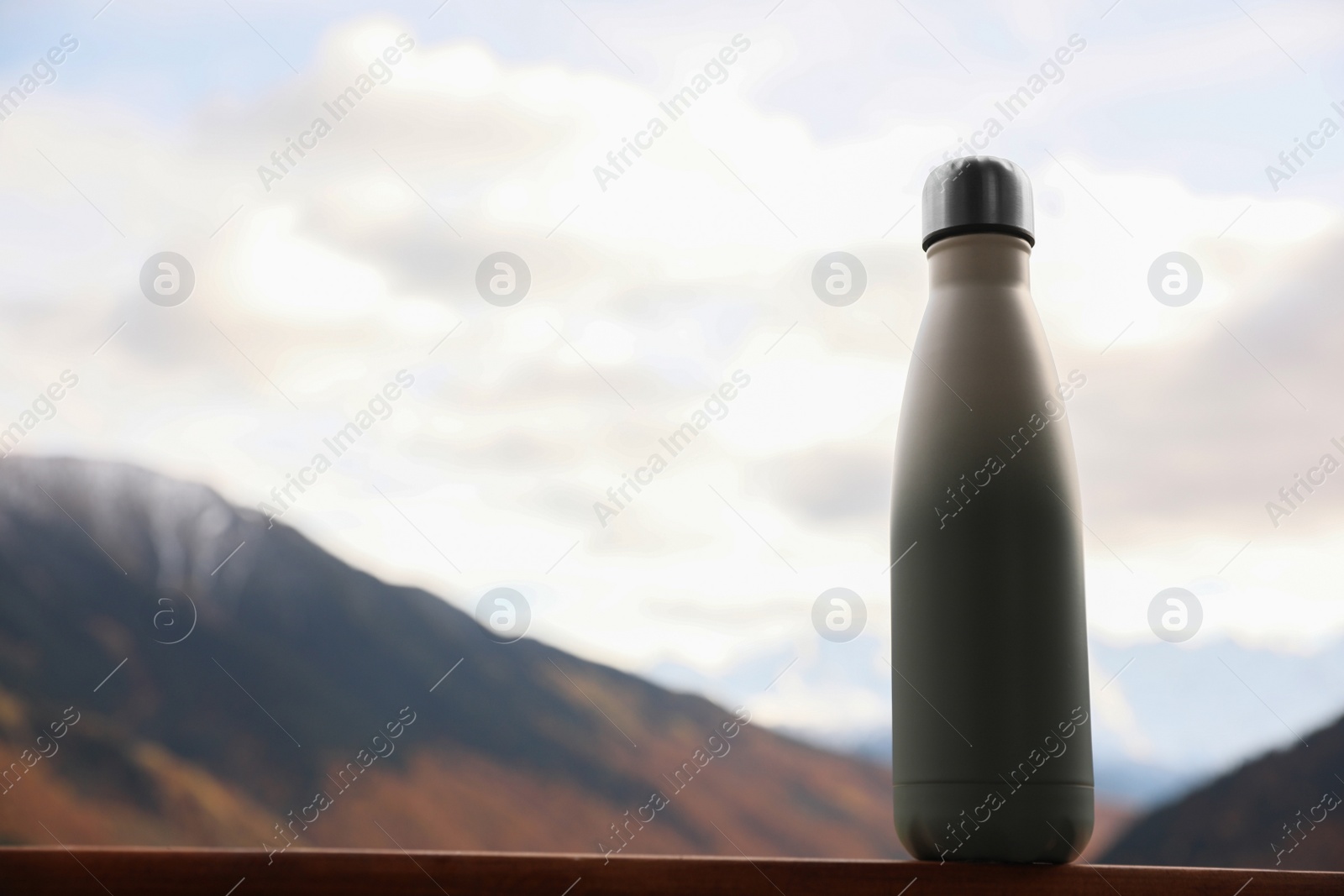 Photo of Thermo bottle on wooden surface in beautiful mountains. Space for text