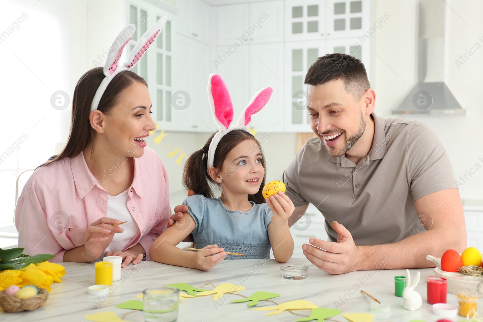 Photo of Happy father, mother and daughter painting Easter egg at table in kitchen