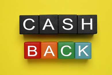 Photo of Word Cashback made with cubes on yellow background, flat lay