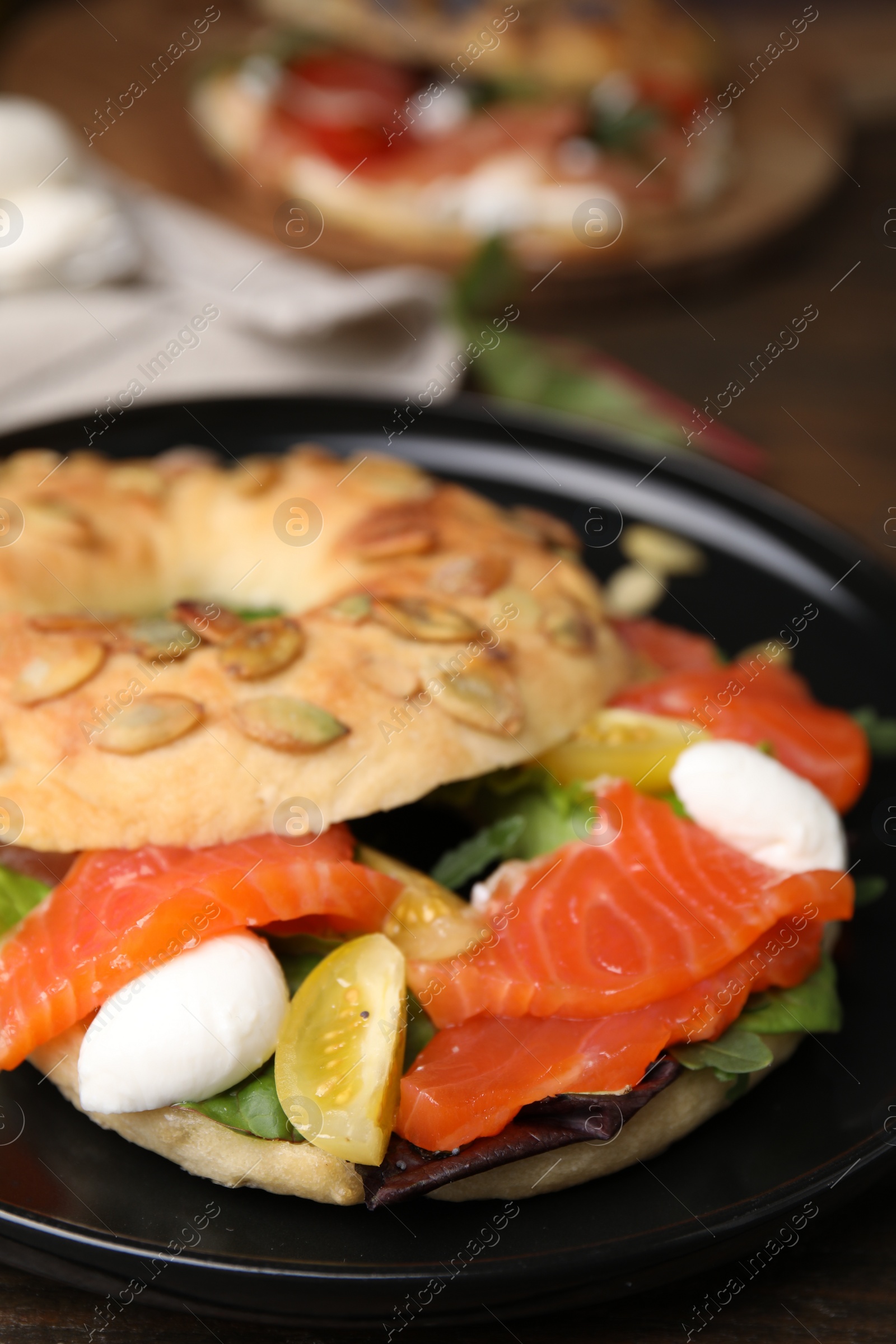 Photo of Tasty bagel with salmon, mozzarella cheese, tomatoes and lettuce on table, closeup