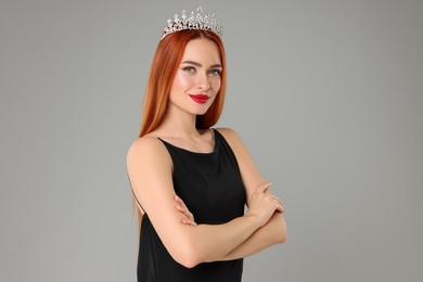 Beautiful young woman with tiara in dress on light grey background