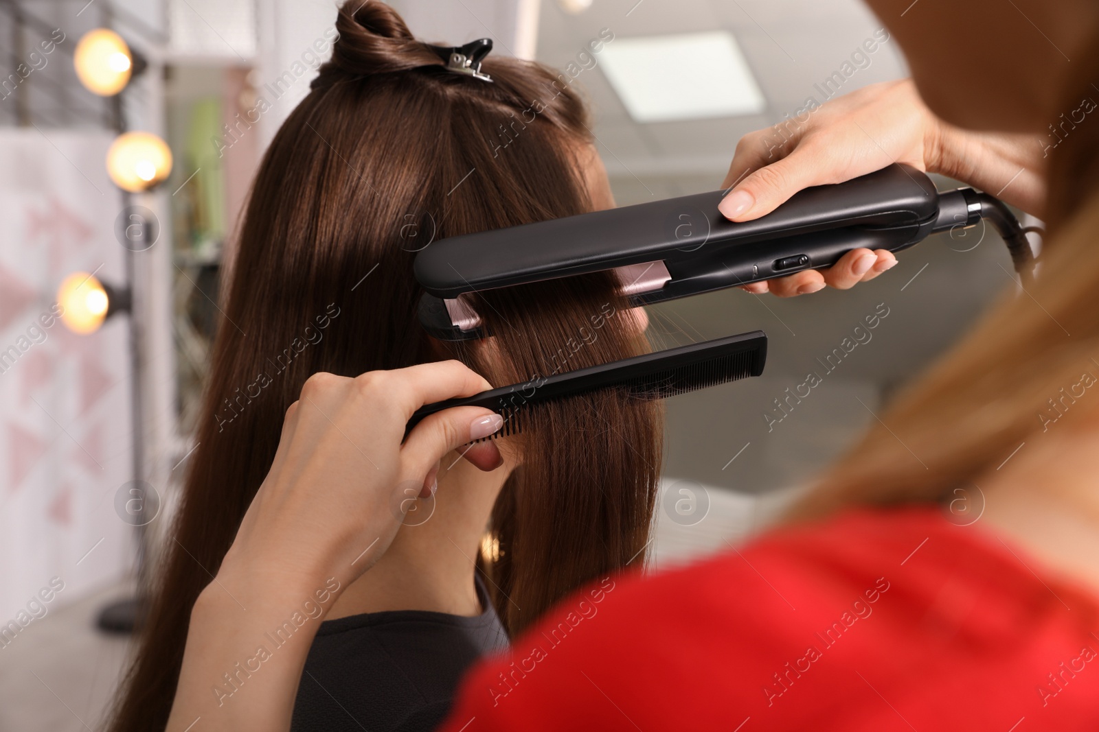 Photo of Stylist straightening woman's hair with flat iron in salon