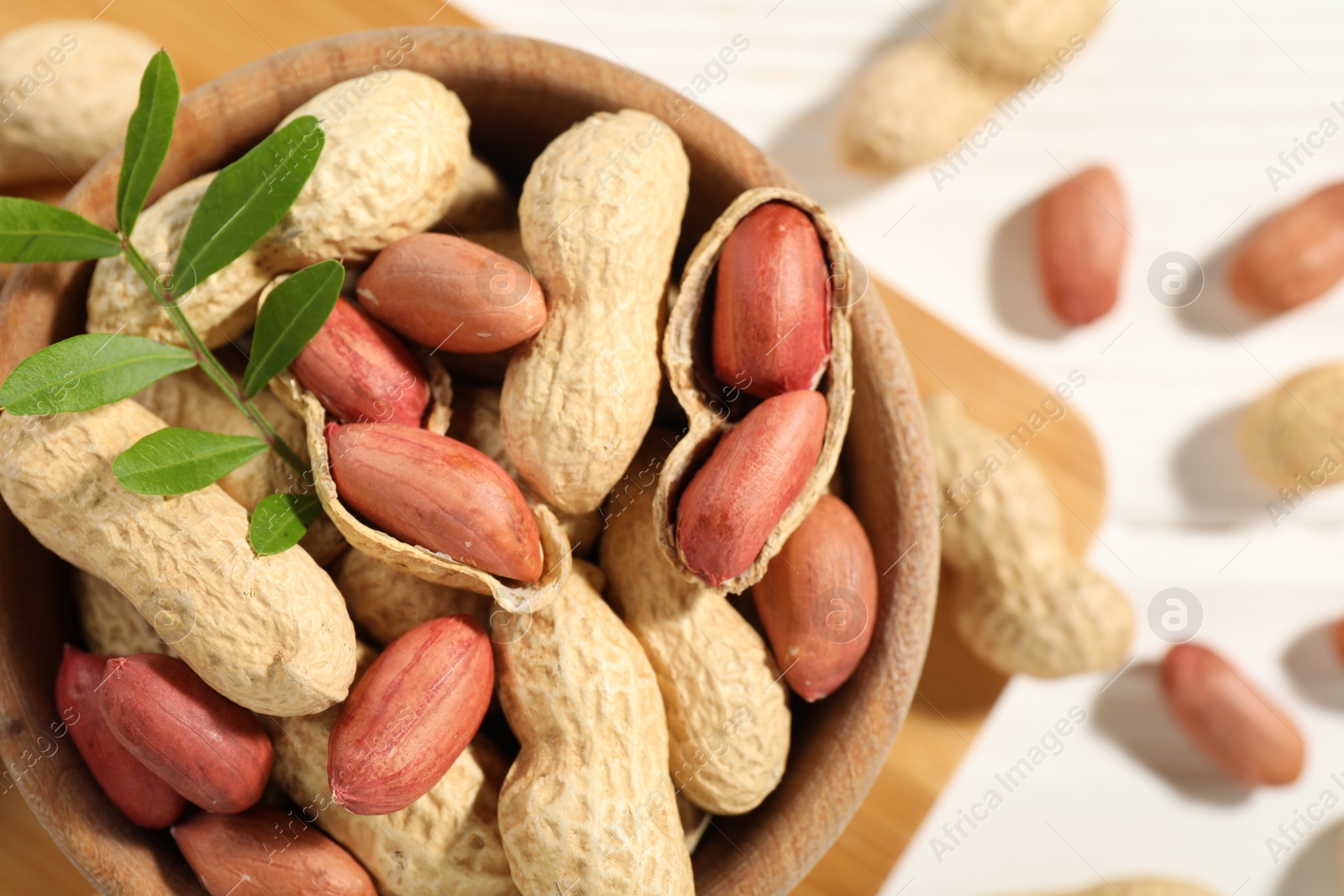 Photo of Fresh unpeeled peanuts in bowl and twig on table, top view