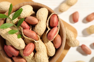 Fresh unpeeled peanuts in bowl and twig on table, top view