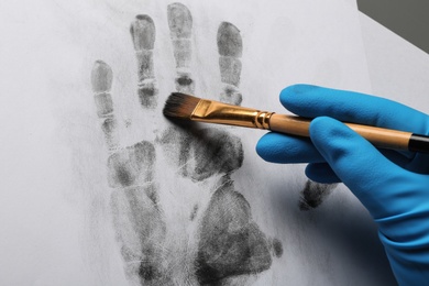 Photo of Detective taking fingerprints with brush from paper on grey background, top view.  Criminal investigation