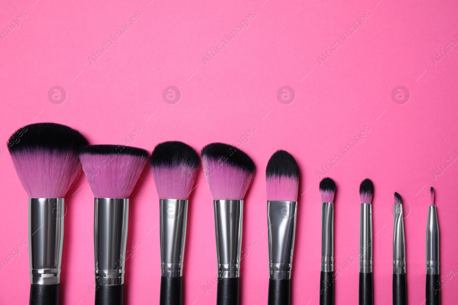 Photo of Set of makeup brushes on pink background, flat lay