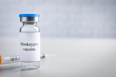 Monkeypox vaccine in glass vial and syringe on white wooden table, space for text