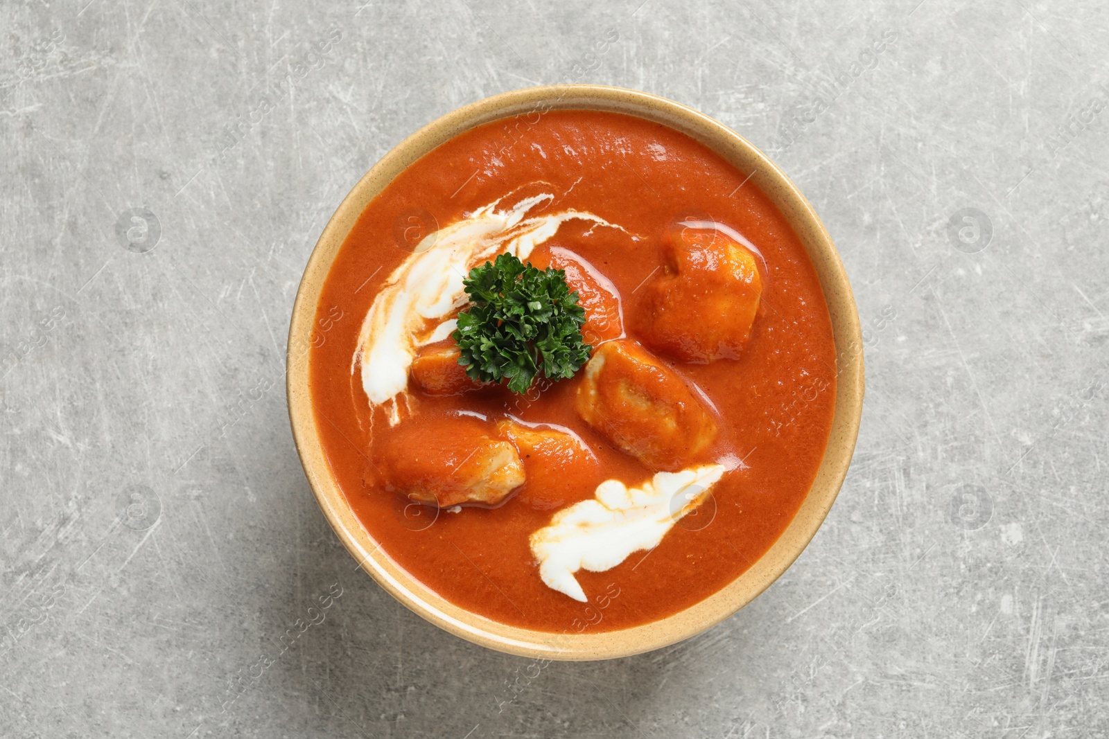 Photo of Bowl of delicious butter chicken on grey background, top view. Traditional indian Murgh Makhani