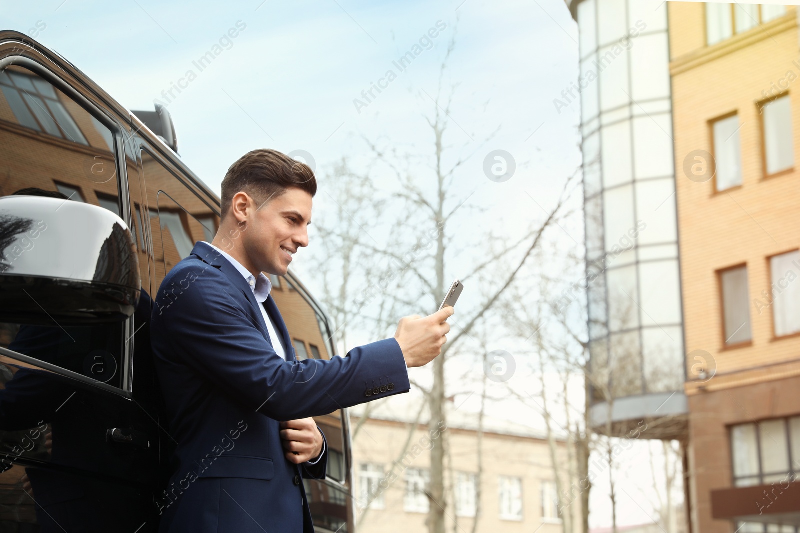 Photo of Handsome man with smartphone near modern car outdoors