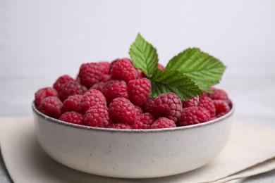 Photo of Bowl of fresh ripe raspberries with green leaves on table, closeup