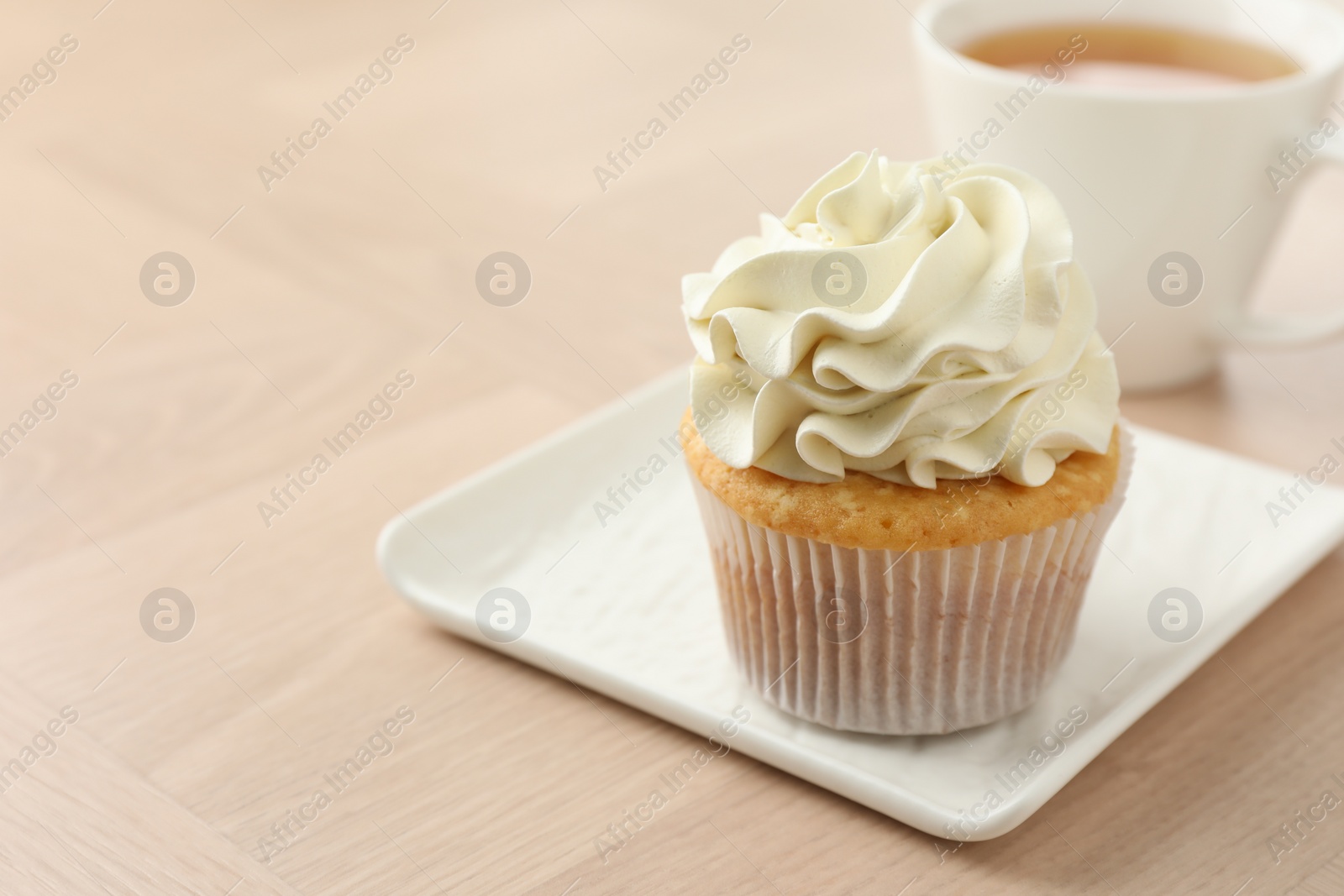 Photo of Tasty cupcake with vanilla cream on light wooden table, closeup. Space for text