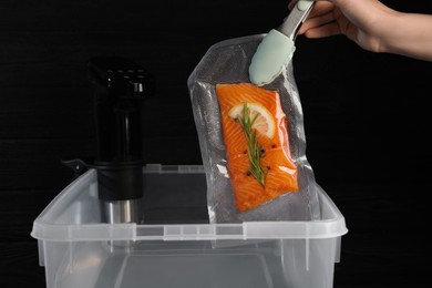Woman putting vacuum packed salmon into box with thermal immersion circulator, closeup. Sous vide cooking