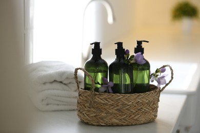 Photo of Wicker basket with soap dispensers , flowers and clean towels on table