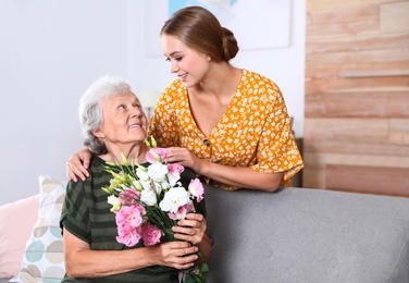 Photo of Young woman congratulating her senior mom at home. Happy Mother's Day